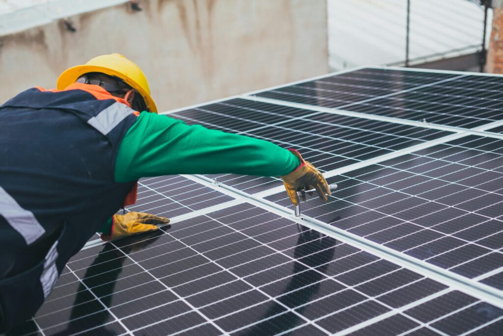 Profissional com capacete e luvas instalando painéis solares, representando os cursos de energia solar do Instituto Aprimore.
