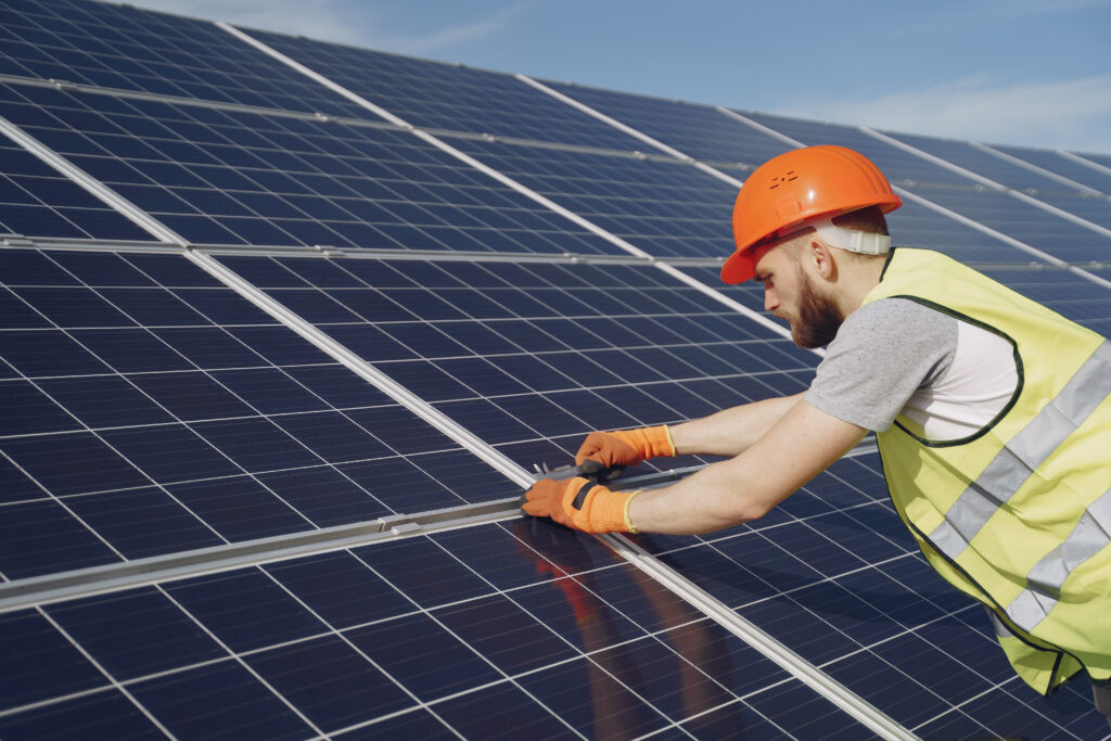 Trabalhador com capacete laranja e colete refletivo ajustando painéis solares, representando o curso Energia Solar – Fundamentos.